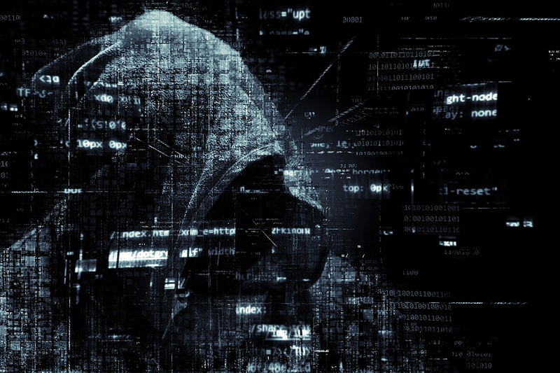 Hooded figure overlaid with streams of code and binary digits on a dark background