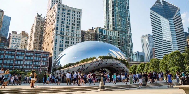 Crowds around Chicago's mirrored Cloud Gate sculpture with skyscrapers behind